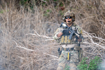 Fototapeta premium Soldier in camouflage uniform aiming rifle gun while kneeling near rock cliff. Tactical military warrior holding weapon during combat training outdoor