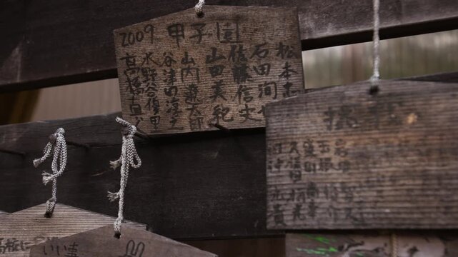 Slow pan across weathered wooden ema prayer plaques with Japanese calligraphy.