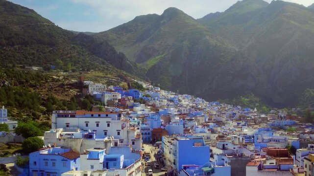 Drone retreats from streets to reveal Chefchaouen blue city and mountains.
