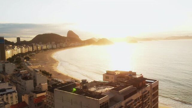 Drone pulls back from Rio rooftops revealing Copacabana Beach at sunset