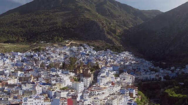 Drone pulls back to reveal Chefchaouen half-shadowed by the Rif peaks