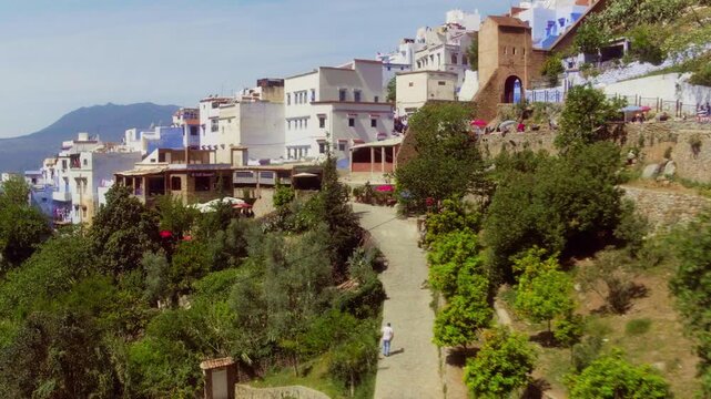 Drone pulls back over Chefchaouen's lush garden path as a man walks up.