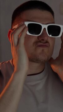 A guy wearing stylish white-framed glasses dances and rejoices in a dark room.
Good mood and dancing