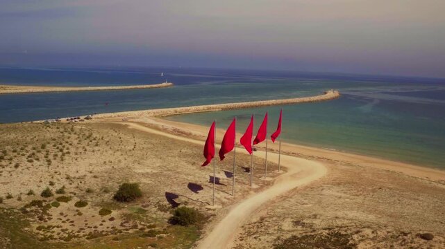 Five red flags stake the sky above Morocco's golden sandy coastal spit.