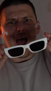 A guy wearing stylish white-framed glasses dances and rejoices in a dark room.
Good mood and dancing