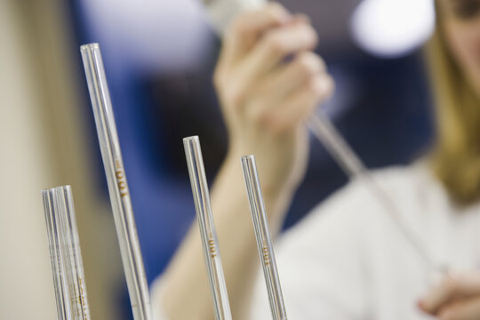 Close-up of four volumetric pipettes with a scientist pipetting in the background