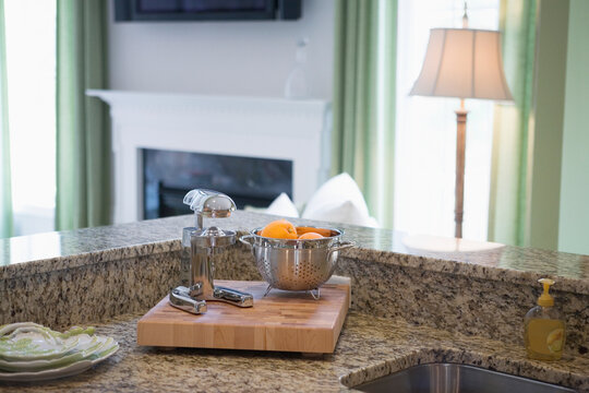 Oranges in a colander near a juicer on a cutting board