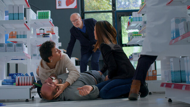 Man strolling through apothecary getting sudden epilepsy attack, fainting and foaming at the mouth, panicked clients trying to save muscle spasms suffering victim twitching on floor