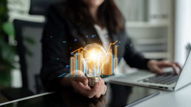 Business Professional Holding Light Bulb with Virtual Financial Graphs in Modern Office Setting, Symbolizing Ideas and Growth Strategies. Entropy.