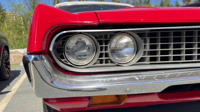 A stunning classic red car catches the eye with its shiny chrome details. Sunlight dances on its surface while vibrant nature surrounds the peaceful parking lot
