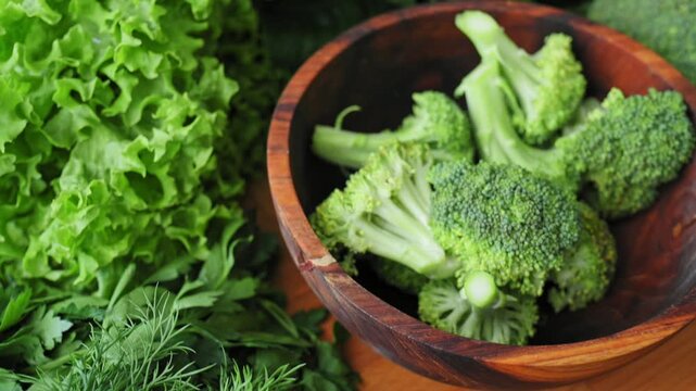 Fresh green broccoli florets in wooden bowl surrounded by leafy greens. Organic, high-quality natural products for healthy lifestyle, farm-raised vegetables.