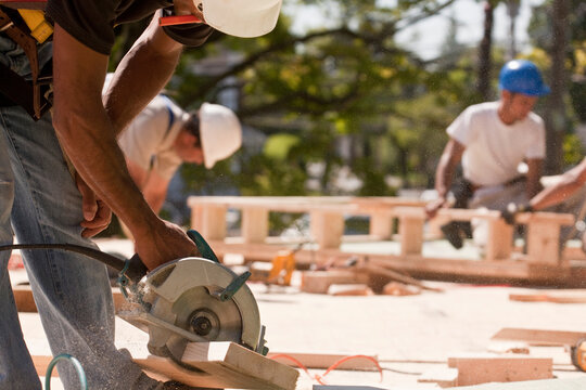 Carpenters using circular saw at a construction site with gable frame in the background