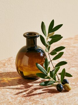 Close up of a single dark glass bottle of premium olive oil with a branch of fresh green olives and leaves on a textured surface