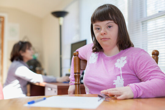 Girl with Down Syndrome sitting on chair with her mother using computer in the background