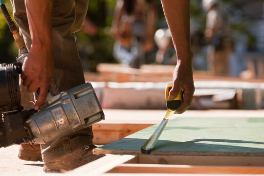 Carpenters holding a nail gun and measuring a board