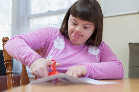 Girl with Down Syndrome cutting a paper with scissors