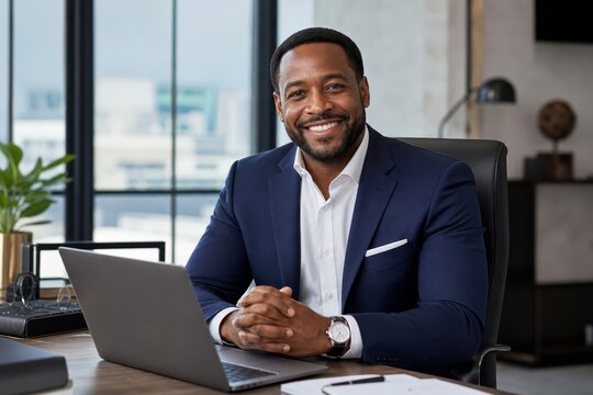 Smiling african american businessman sitting at a desk with a laptop in a modern office