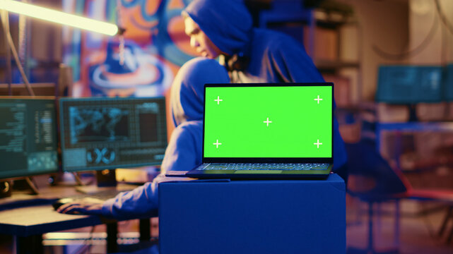 Green screen laptop in bunker with graffiti walls left behind by hackers to act as decoy. Mockup device running script pinging wrong location to cybercriminal law enforcement chasing them.