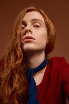 Elegant young man with long red hair and captivating style poses gracefully in rich colors