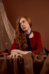Obraz premium Handsome young man with long red hair embodies elegance in stylish attire on a rich backdrop