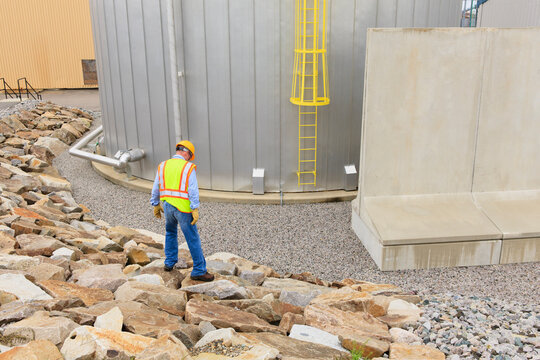 Engineer at electric power plant standing near water storage tank