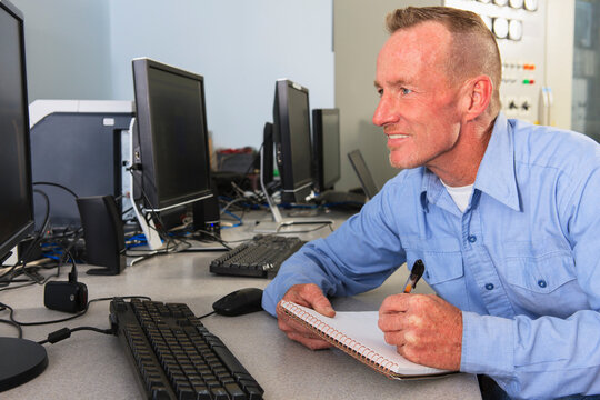 Engineer at electric power plant control room recording a log at management displays