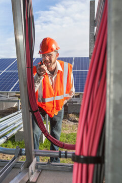 Power engineer talking on radio while looking at power cabling at solar photovoltaic array