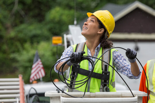 Hispanic female cable lineman stringing a new line in the rain