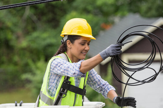 Hispanic female cable lineman stringing a new line in the rain