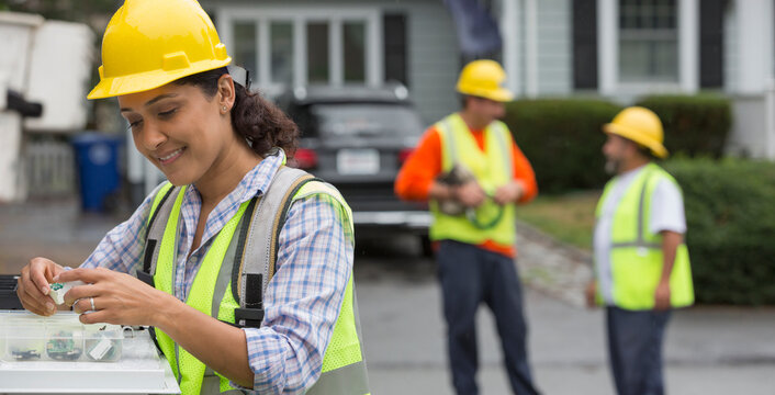 Hispanic female utility worker with box of cable amplifiers at site