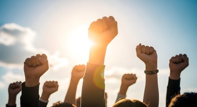 Group of people raising fists in solidarity against a bright sunny sky