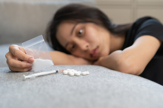 Anti drugs, drug addict asian young woman, girl hand holding heroin or cocaine in plastic bag, use narcotic at home, abuse overdose. Sick pain of health, unhealthy people. Suicide depressed or despair