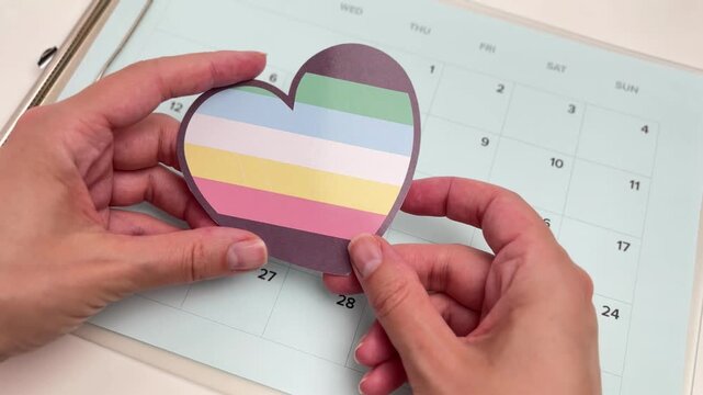 Hand placing a heart with the Disability Pride flag colors on a calendar, inclusivity and awareness concept