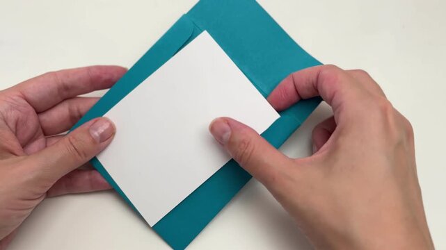 Hand putting a white greeting card into a blue envelope on a white background