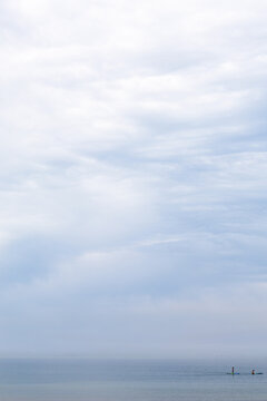 Calm sea and cloudy sky with distant paddle boarders.Calm beach scene with two people paddle boarding on a still sea under a soft cloudy sky. Peaceful coastal view with gentle waves, wet sand, and lot