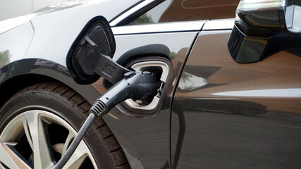 Fototapeta premium Close-up of electric car charging battery with power cable supply at station. Macro shot of modern EV plug connected to black hybrid automobile