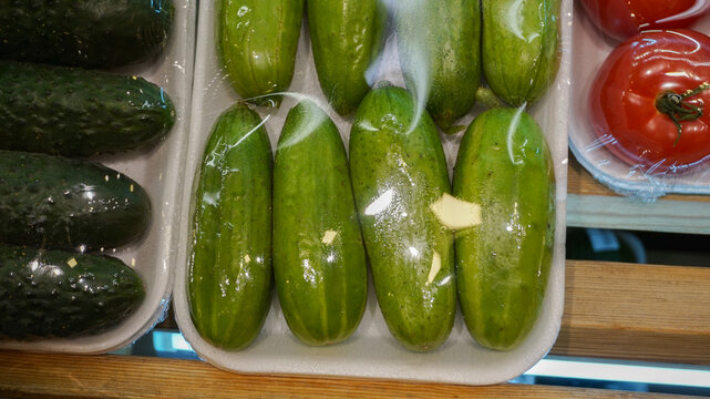 Close-up of fresh green cucumbers packed in a white styrofoam tray and wrapped in clear plastic film for sale on a grocery store shelf.