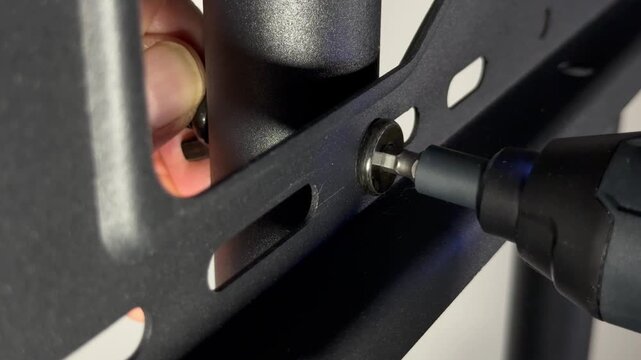 Closeup of a man&rsquo;s hands using a power drive tool with hex tip fitting, while holding a wing nut, to release a bolt which is holding parts of a metal frame together.