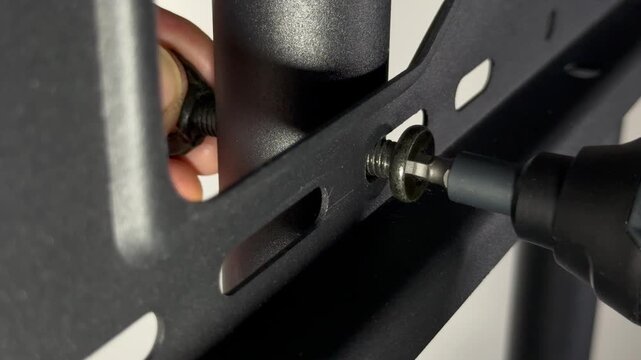 Closeup of a man&rsquo;s hands using a power drive tool with hex tip fitting, while holding a wing nut, to fasten a bolt and join together parts of a metal frame.