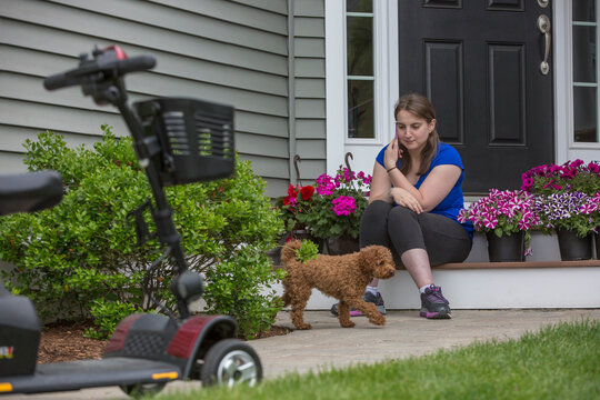 Woman sitting on porch steps with a small dog, surrounded by vibrant flowers
