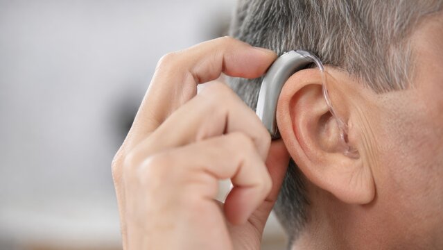 Close-up of a person fitting a behind-the-ear hearing aid to their ear, showing hand adjustment and ear detail
