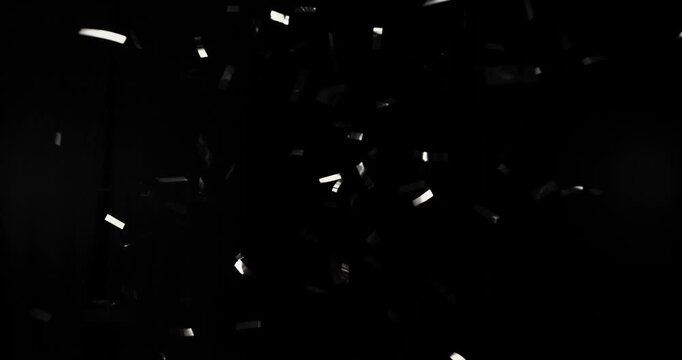 Silver confetti flying in super slow motion against a black background. Shiny metallic particles drifting and falling in the air, creating elegant festive atmosphere with dramatic lighting.