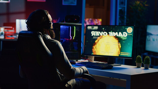 Upset gamer hitting desk in frustration after receiving game over screen, getting his spaceship destroyed in flying game, sad player feeling disappointed after losing science fiction videogame.