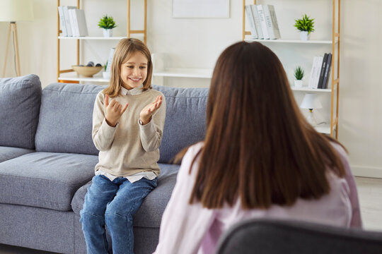 Happy kid speaking with therapist or psychologist on home counseling session, behavior therapy. Child smiling with trust, sitting on sofa, looking at teacher listening with support and empathy