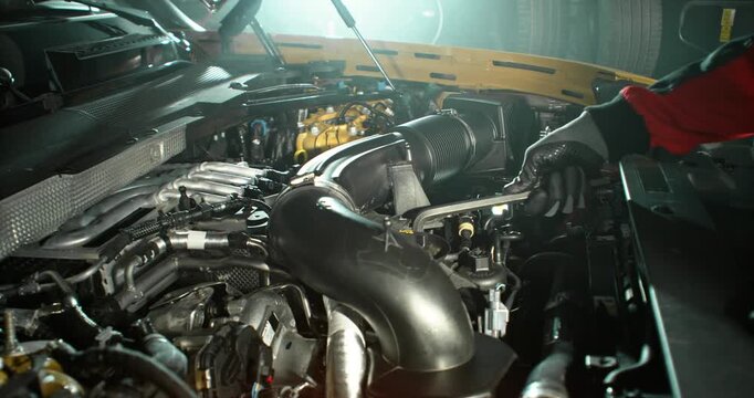 Slow motion shot of mechanic working on car engine with camera movement above engine, dramatic lighting in workshop. Automotive repair concept, maintenance and service.