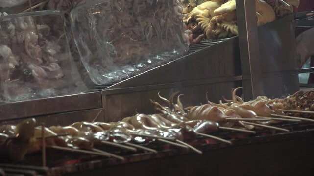 Slow-motion footage of squid being grilled as street food in Bangkok, Thailand.