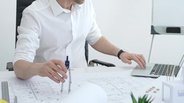 Architect drawing building plans on blueprints using a compass, creating a new construction project design, working on engineering and drafting tasks in an office