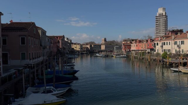 Sunny Italian canal with moored boats and city skyline
