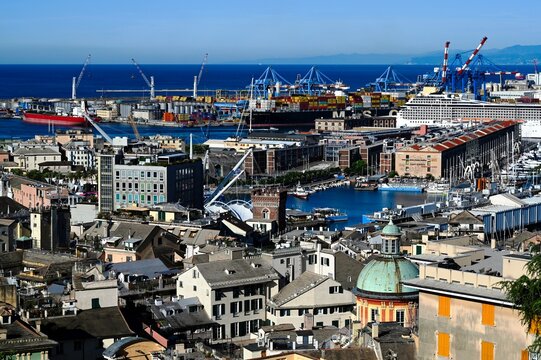 aerial view of Central Genoa old port area. rooftops and stucco facades. heavy duty harbor cranes at far. copper dome of church. deep blue sea at the horizon. travel and tourism 