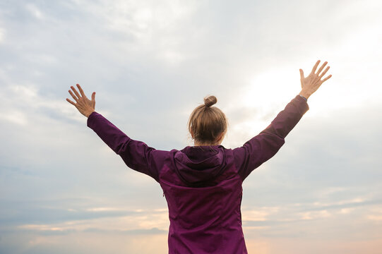 Coastal freedom woman rises hands beneath dramatic clouds